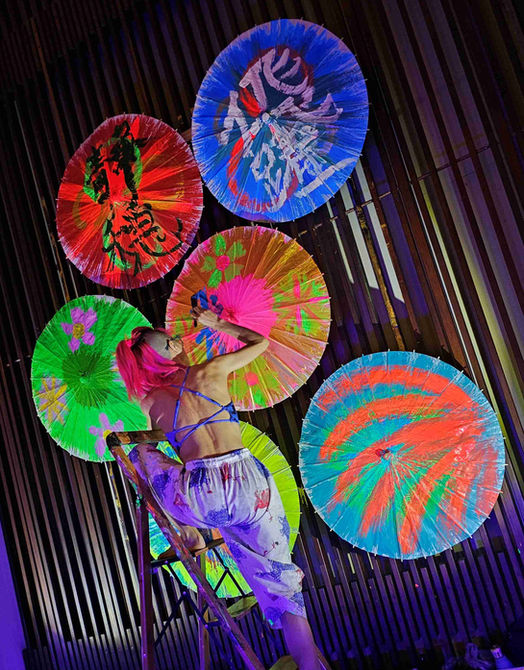 Japanese calligraphy artist painting a paper umbrella collage with bright colors.