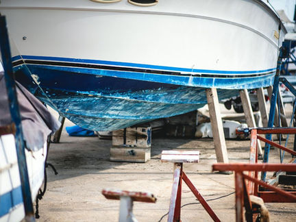 A white and blue boat on wooden supports in a shipyard, surrounded by other equipment. The scene has a rustic, industrial feel.
