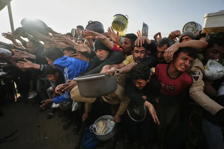 Displaced Palestinians struggle to receive donated food for iftar, the fast-breaking meal, on the first day of the Muslim holy month of Ramadan at a community kitchen in Khan Younis, the Gaza Strip, on February 18, 2026 [Jehad Alshrafi/AP]