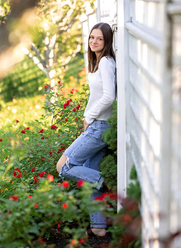 High school senior leaning against white fence at Pineland Farms in New Gloucester