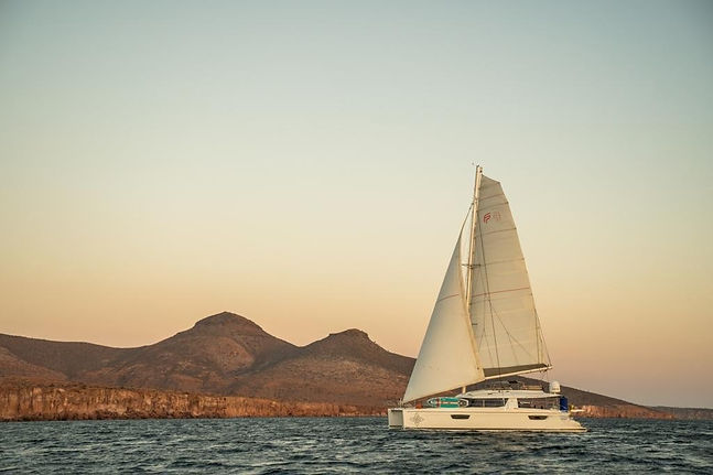 White sailboat sailing on the ocean with mountains in the background.