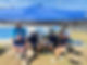 Staff sitting under a blue tent at an outdoor program.