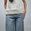 Miniatura: Woman wearing a white top with fur trim and denim jeans, standing inside.