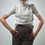 Miniatura: Woman wearing a beige turtleneck sweater and brown pants, hands in pockets.