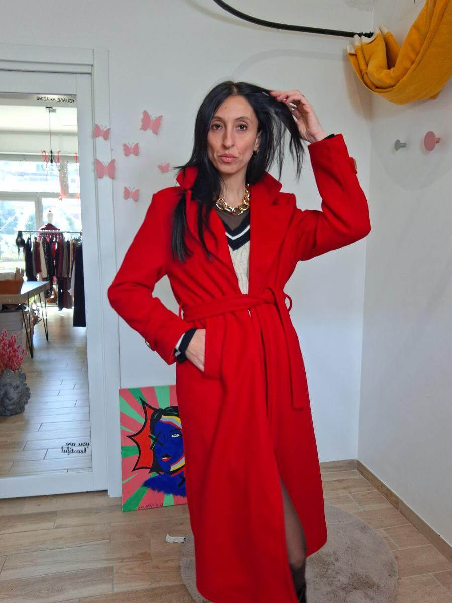 Una donna in cappotto rosso, in una stanza, che si tocca i capelli.