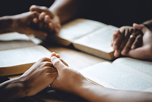 Christian group of people holding hands praying worship to believe and Bible on a wooden t