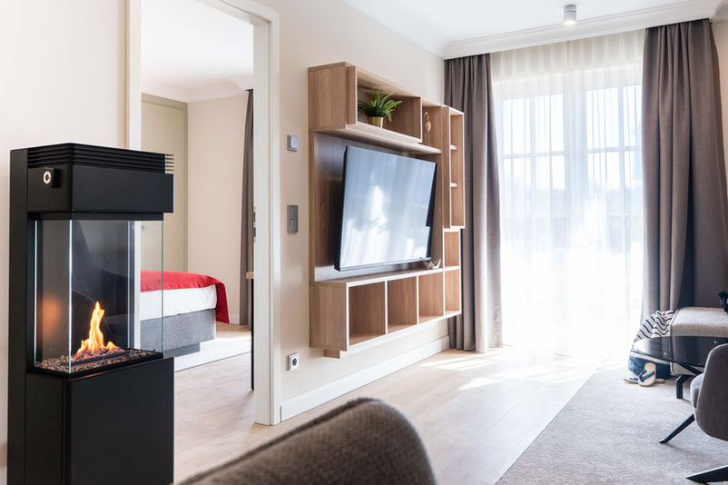 Gemütliches Wohnzimmer mit Kamin, Fernseher und Schlafzimmer im Hintergrund Ferienwohnungen Ostsee.