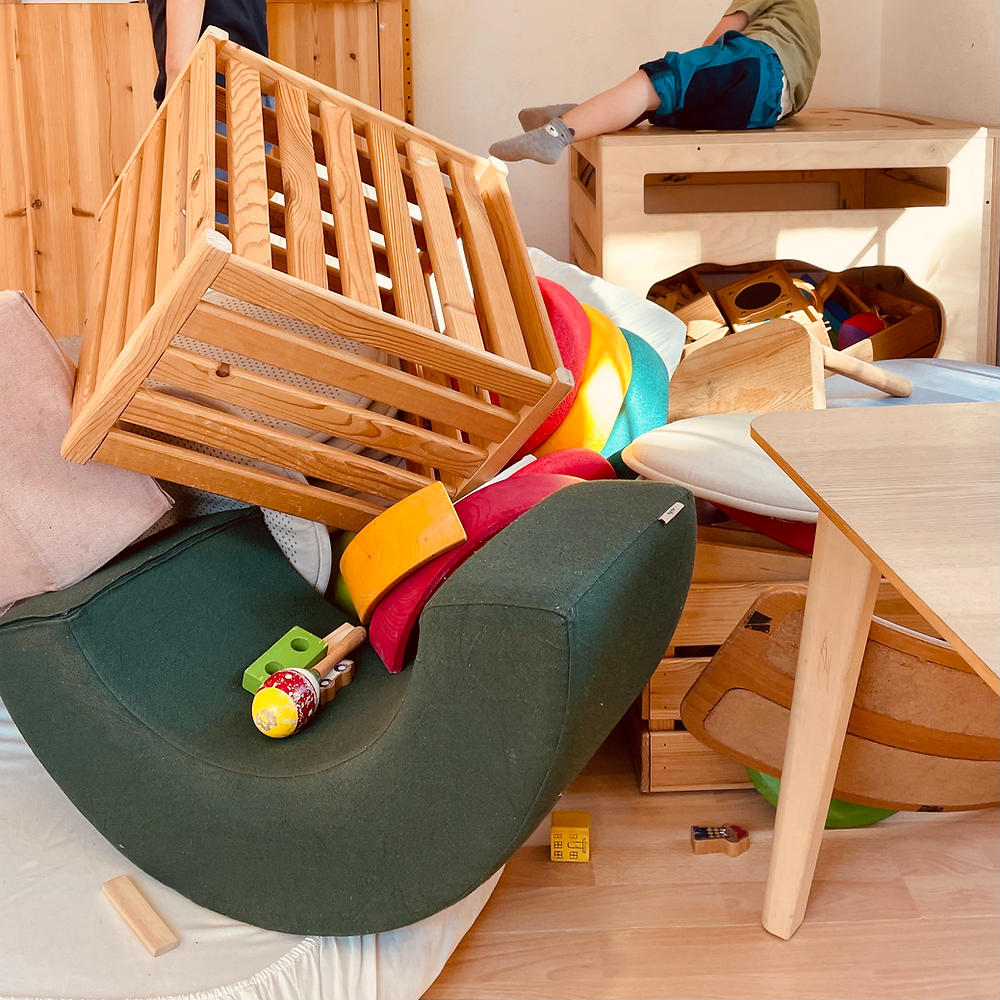 Ein Ausschnitt eines kreativen, freien Spiels, in welchem die Kinder diverse Materialien wild kombiniert haben (Stoffblöcke, Matten, Kisten, einen Kindertisch und diverse Holzspielsachen).