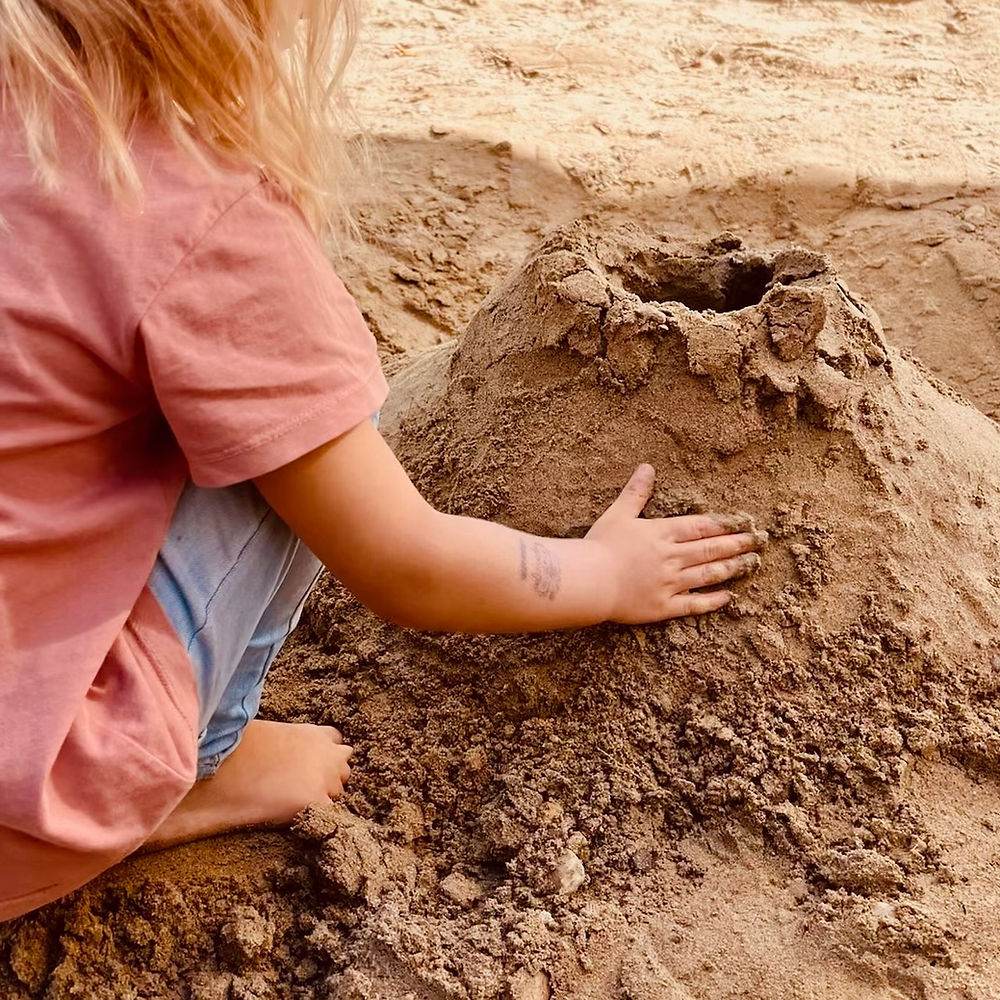Ein Kind baut eine Sandburg im grossen Sandkasten der Kita.
