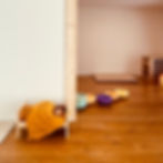 Raum für Freispiel und Bewegung mit Holzelement zum Klettern, Stapelsteinen zum Balancieren und Spielen, einer Matte und zwei Puppen in einem Puppenbett.