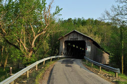 Rustic wooden covered bridge at the end of a paved road.