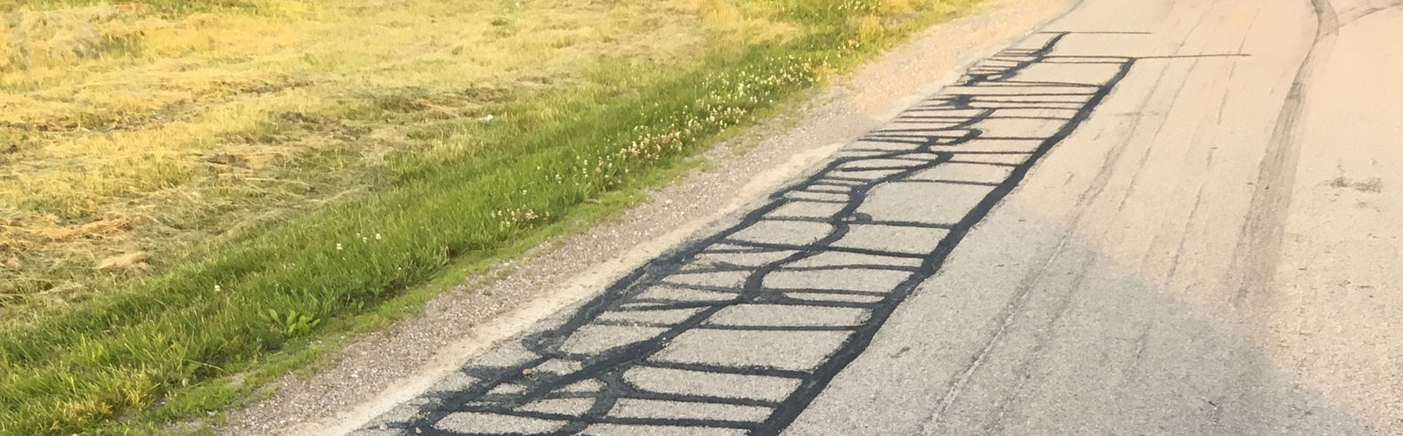 Cracked asphalt road with patched areas and green grass beside it