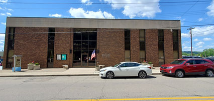 Brick building, glass entrance, American flag, white sedan, red SUV