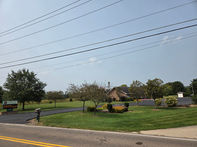 Green lawn with trees and a building Harrison TWP under a blue sky.