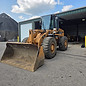 Orange front loader parked near a building on a cloudy day.
