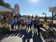 Group of seniors stand outside on a sunny day near a building.
