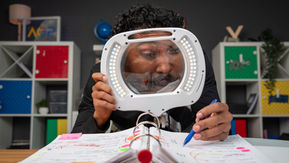Person using an illuminated magnifying glass to review Chromebook repair records for recurring patterns.