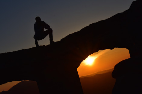 Silhouette of man crouched ontop of a rock pillar with a dark night sky ontop and a bright orange sunset below