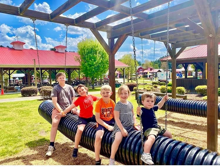 Five young boys happily sitting on black play pipes at outdoor attraction.