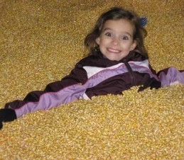 Young girl smiling happily while lying in a large corn pit.