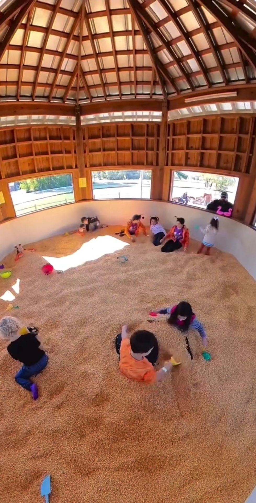 Children playing in a large covered cornpit under a wooden structure.
