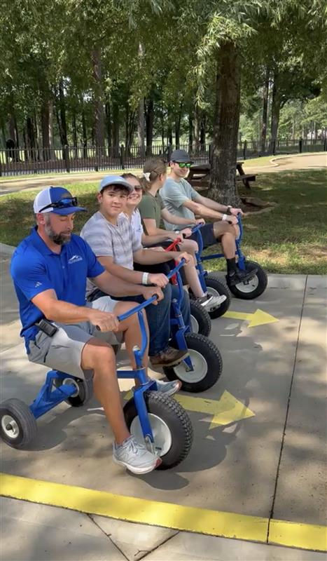 Adult and two kids riding tricycles, an outdoor attraction