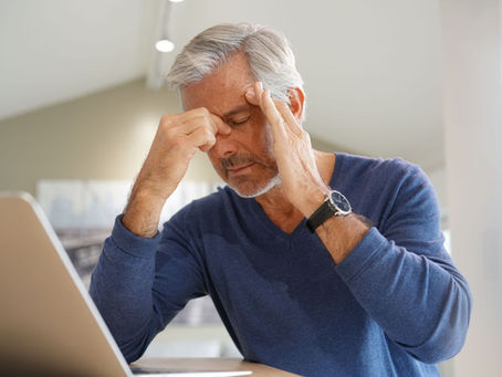 Man rubbing his forehead and temple while sitting at a laptop with a tension-type headache