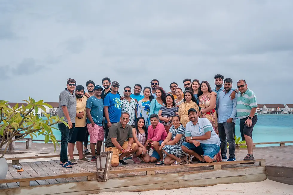 Office group posing on a wooden deck with tropical water and bungalows