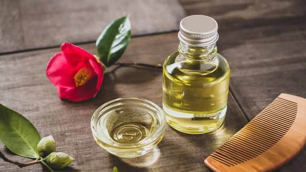 Glass bottle and bowl of oil with a wooden comb on a wooden surface. A red flower with green leaves adds color to the serene setting.