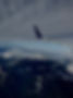 Airplane wing soaring over snow-capped mountains and vast cloudy skies.