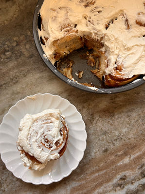 freshly baked homemade cinnamon rolls with cream cheese frosting on a plate and pan filled with cinnamon rolls