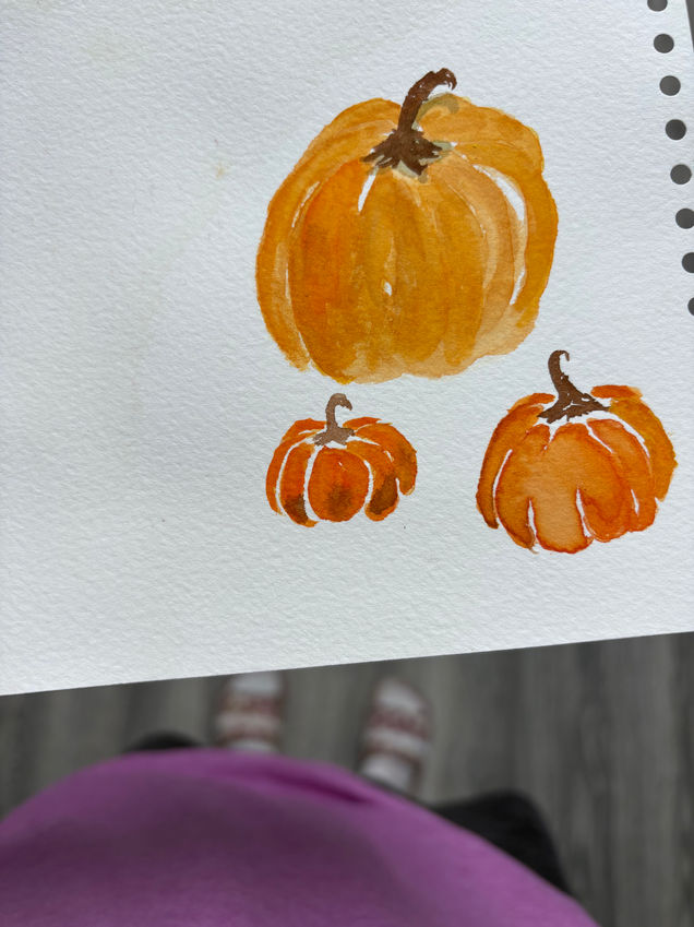 Beginner watercolor painting of pumpkins in various shapes and colors, exploring color blending and texture on cold press paper.
