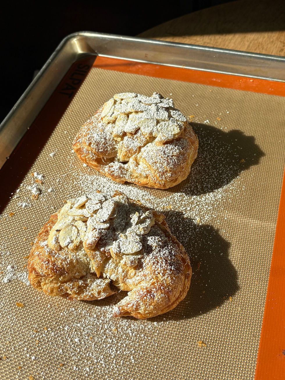 Close-up of homemade almond croissants with powdered sugar and almonds catching the morning sun.