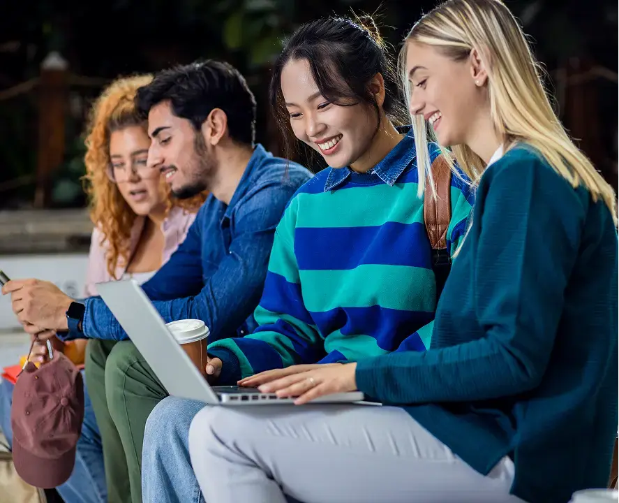 Four diverse students smiling and looking at a laptop.