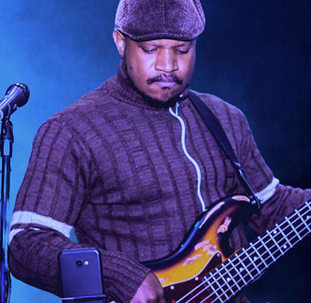 Elizeu cruz de boina e casaco, olhando para baixo e tocando seu contrabaixo elétrico.