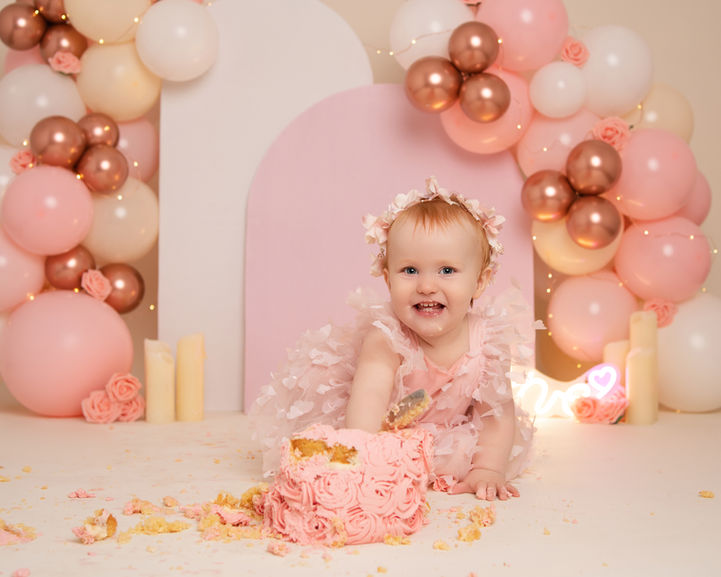 One-year-old enjoying pink cake smash with soft pastel balloon styling
