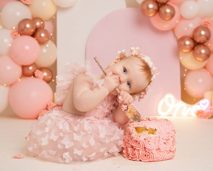 Baby girl lying beside cake in blush pink cake smash photoshoot
