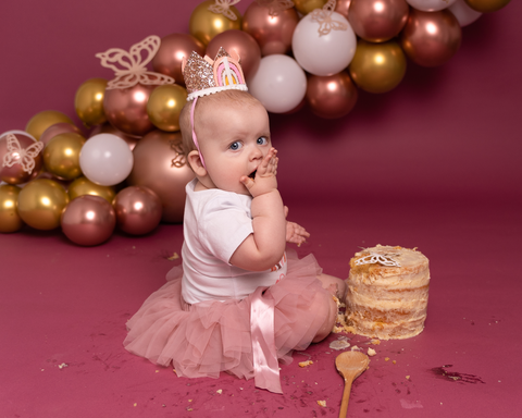 Baby girl seated with balloon arch during cake smash