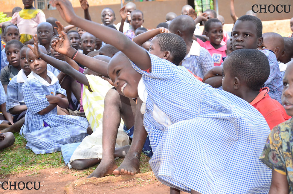 Ugandan primary school children raising their hands in class during CHOCU tuition and supplies program, promoting education access for low-income families.