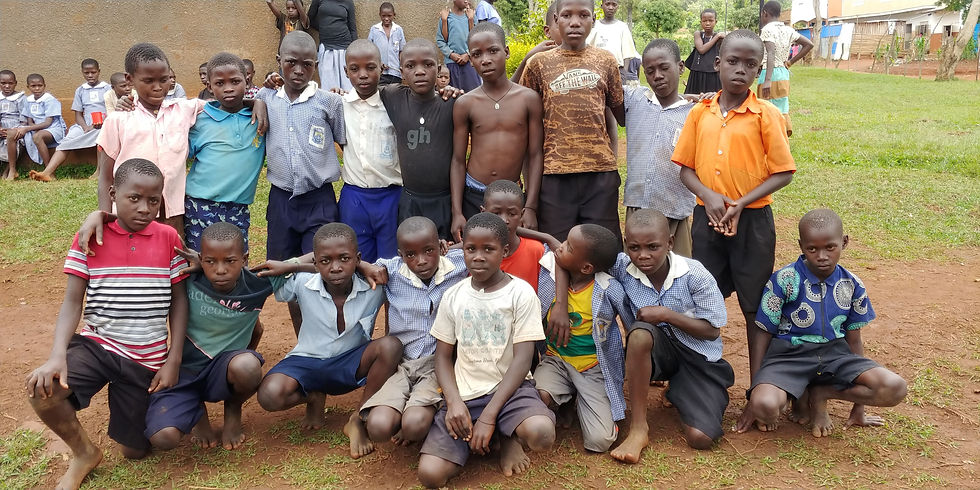Group of school-age boys in rural Uganda posing for a photo outside, smiling and standing together on a dirt field, representing children supported by CHOCU.
