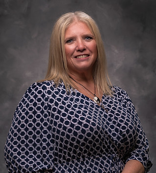 Woman with blonde hair wearing a patterned top, smiling on a grey background.