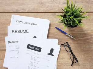 CV's on a desk with a pen, a pair of glasses and a green spiky plant next to them