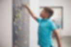A boy in a turquoise shirt reaches for colorful magnetic letters on a blackboard in a bright room, focused and engaged. He is participating in a multisensory spelling activity.