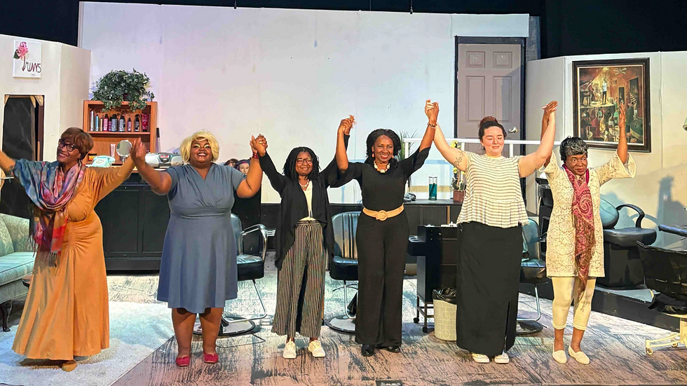 Six women hold hands and smile on stage, acknowledging applause in a salon-themed setting. A sign reads “Junns” above a shelf. steel magnolias cast