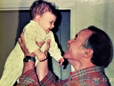 A smiling Allan Shedlin raises a baby, his smiling 1st grandchild, to look her in the eyes.