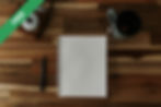 A notepad, pen and camera on a wooden table