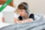 A boy wearing headphones lying on a bed
