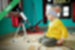 A young boy sitting on the floor next to a telescope