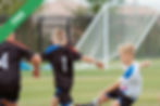 Three children playing football on a grass field