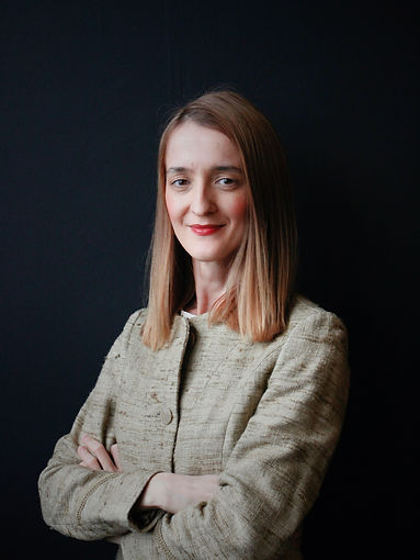 Jelena Petrovic - Co-Founder - Young female in green jacket posing in front of a black wall.